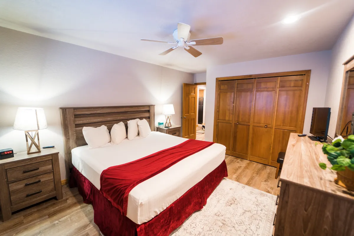 A spacious bedroom with a neatly made bed, flanked by nightstands, a dresser, and a closet. The room is well-organized and filled with soft lighting, reinforcing a sense of comfort and relaxation for guests.