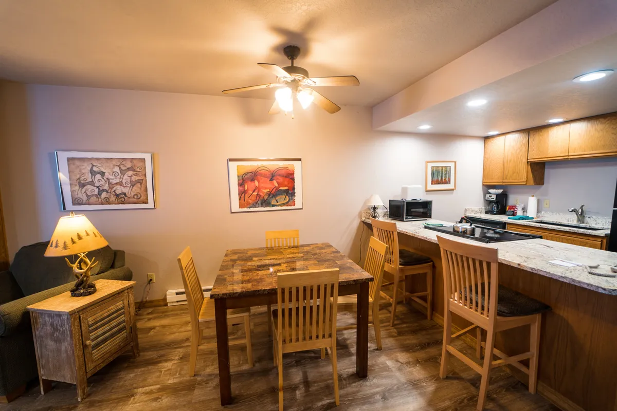 A cozy interior view focusing on a beautifully set dining table positioned near striking artwork and a visible kitchen island in the background. The scene is set for both dining and socializing, with an ambiance of comfort and homeliness.