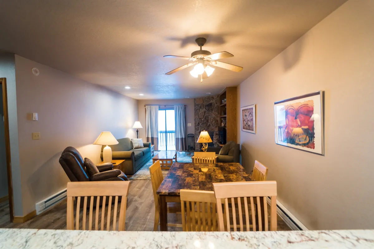 A cozy, wood-accented interior features a large dining table, comfortable seating, and a window with curtains offering natural light. The scene suggests a welcoming spot for family meals, game nights, or relaxing after a day of adventure.