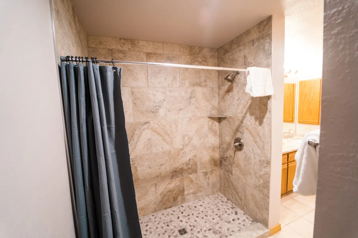 A modern ensuite bathroom featuring a sleek shower area lined with textured stone walls and fluffy, soft towels within reach. The ambiance is fresh and inviting, encouraging relaxation and rejuvenation after a day outdoors.