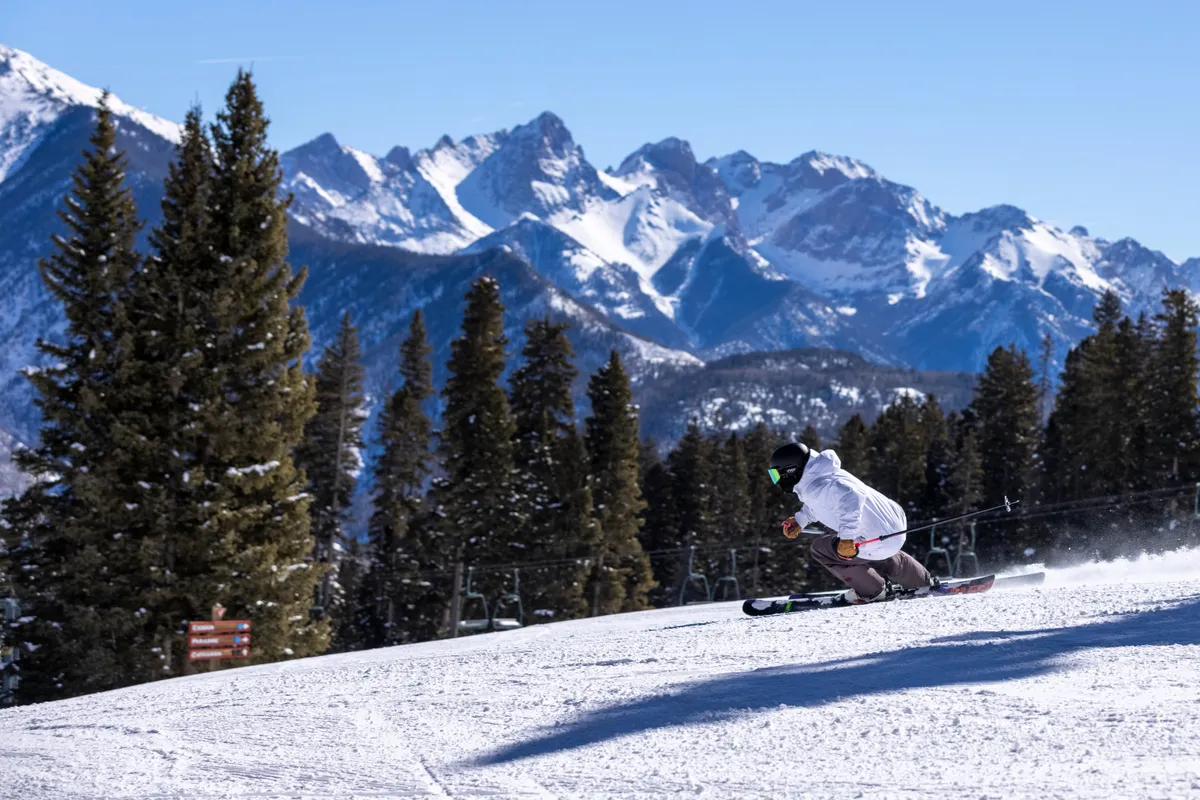 A striking action shot of a skier descending a snow-covered slope with majestic mountains rising in the background. The panoramic winter landscape accentuates adventure and the thrill of winter sports right outside your door.