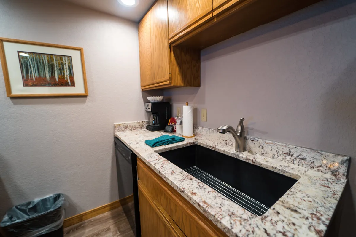 A cozy, stylish kitchen area with a granite countertop, sink, coffee maker, and cheerful artwork. The setup invites guests to gather, cook, and socialize, echoing the comforts of home within a vacation setting.